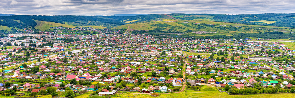 Panoramic view from hill to plain with small town in summer cloudy day. Picturesque urban landscape with many colorful houses. Sim, Chelyabinsk region, Russia. Travel blog concept