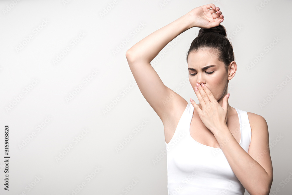 shocked woman looking at underarm and covering mouth with hand isolated on grey shocked woman looking at underarm and covering mouth with hand isolated on grey