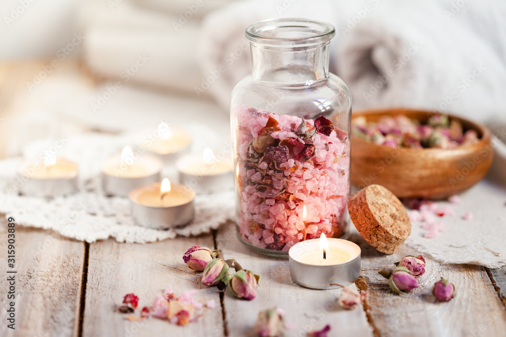 Concept of spa treatment with roses. Crystals of sea pink salt in bottle, candles as decor. Atmosphere of relax and pleasure. Anti-stress and detox procedure. Luxury lifestyle. Wooden background Concept of spa treatment with roses. Crystals of sea pink salt in bottle, candles as decor. Atmosphere of relax and pleasure. Anti-stress and detox procedure. Luxury lifestyle. Wooden background