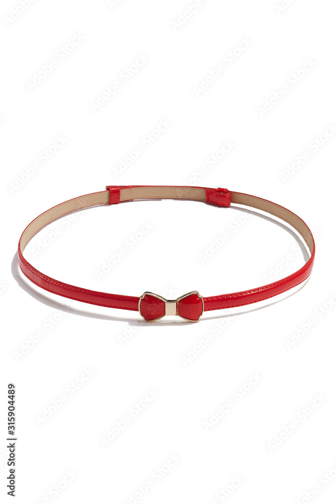 Subject shot of a thin belt made of red patent leather and decorated with a figured buckle in the form of a red enamel bow-knot in golden setting. The stylish belt is isolated on the white background. Subject shot of a thin belt made of red patent leather and decorated with a figured buckle in the form of a red enamel bow-knot in golden setting. The stylish belt is isolated on the white background.
