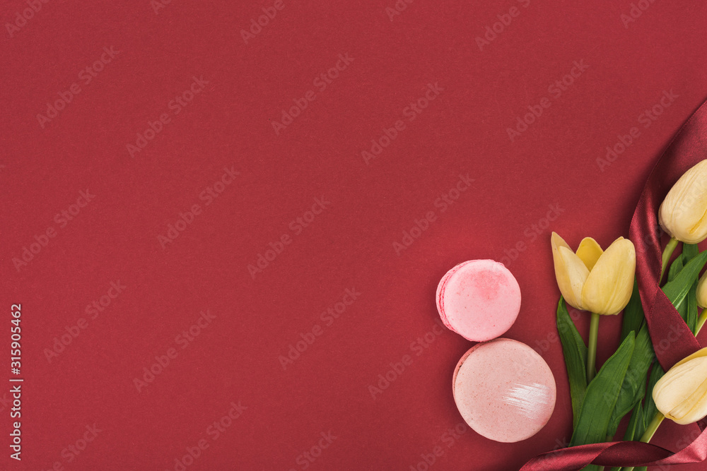top view of tulips with silk ribbon and pink macarons isolated on red top view of tulips with silk ribbon and pink macarons isolated on red