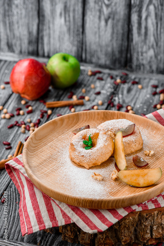 Apple donuts decorated with mint on round wooden plate on red striped napkin on gray wooden background