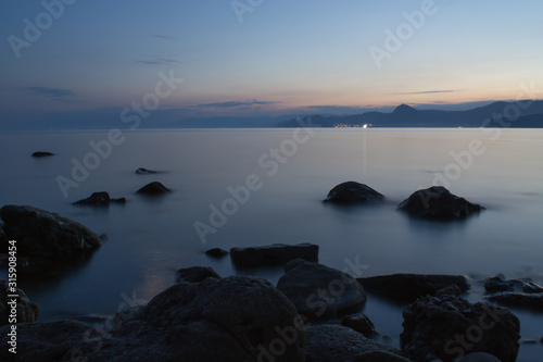 Sea at dusk. Stones on the shore and mountains in the distance.  Sea and mountains after sunset. Photo in the dark. Fog on the water.