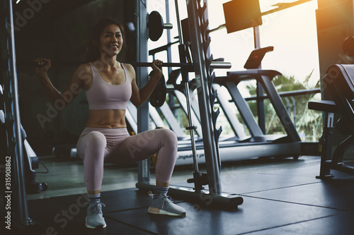 Happy and enjoying of fit woman exercising, her doing exercise with doing squats with a barbell in gym blurred background, ,concept for exercising, health care