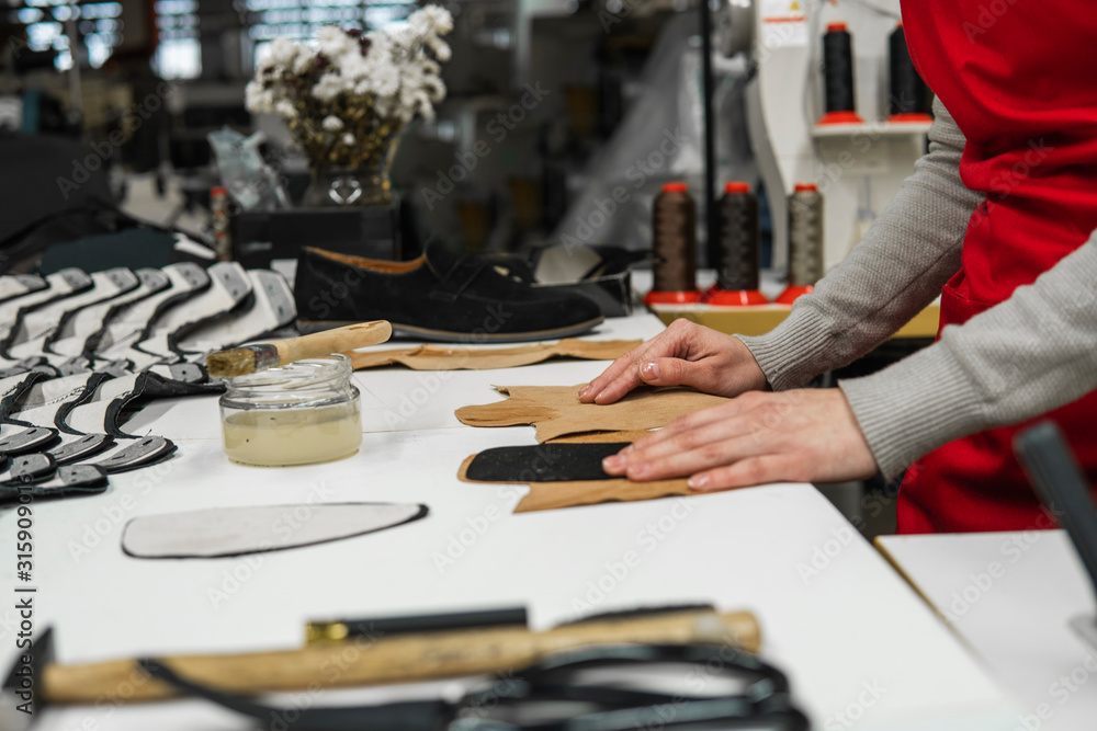 Shoemaker is adding glue with a brush to some pieces of leather that will be used to make shoes. The cobbler is working on his desk in his workshop. Shoemaker is adding glue with a brush to some pieces of leather that will be used to make shoes. The cobbler is working on his desk in his workshop.