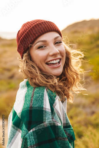 Image of young woman wearing hat and plaid shirt walking outdoors