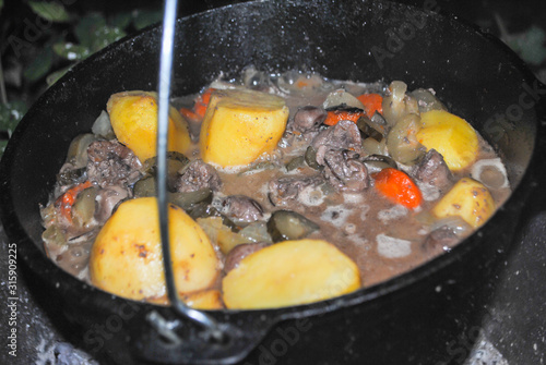 meat and offal with potatoes in a cauldron cooking on a camping trip