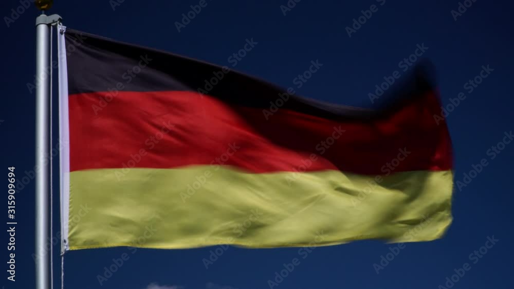 Germany Flag flying in the wind outdoors with Blue sky behind - German flag on flagpole. Germany Flag flying in the wind outdoors with Blue sky behind - German flag on flagpole.