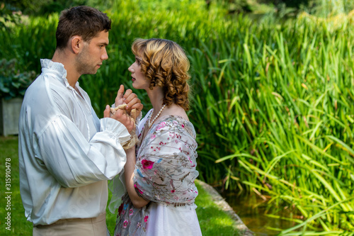 Fotografie Young handsome couple dressed in vintage costume standing on embankment by river
