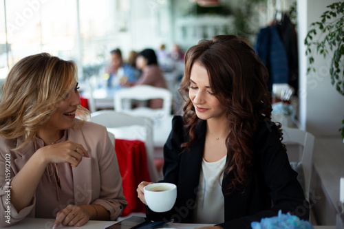 Two femlae friends sit in elite restaurant with a beautiful view of the sea, women drinks coffee. The female person wearing white shirt. Girl waiting the order and communicates.