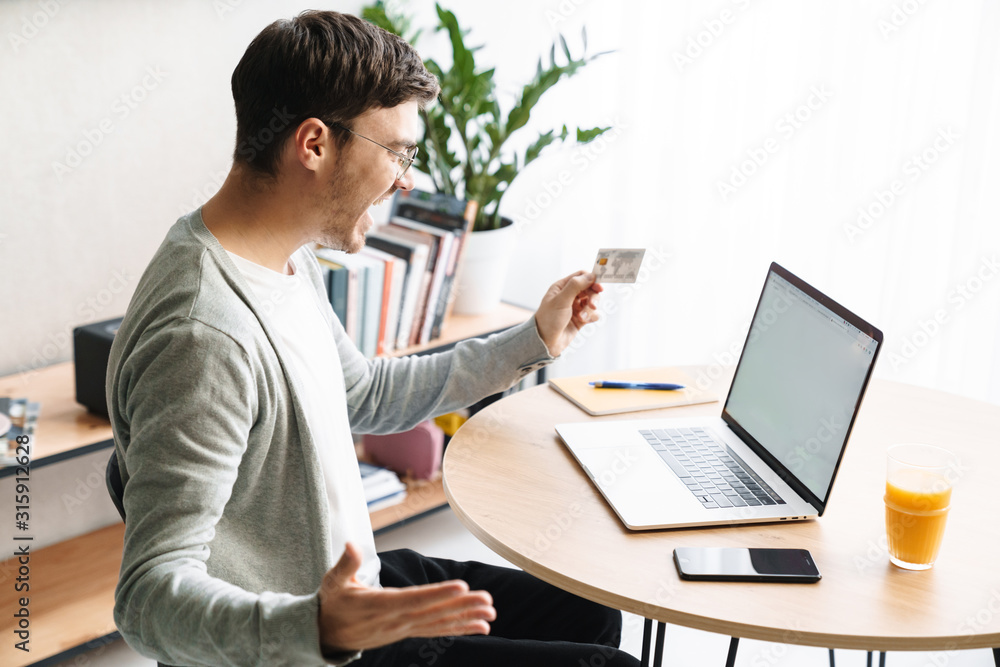 Image of man holding credit card while making payment with laptop at home Image of man holding credit card while making payment with laptop at home