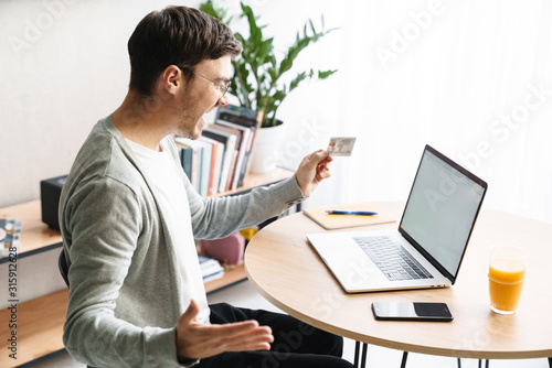 Image of man holding credit card while making payment with laptop at home
