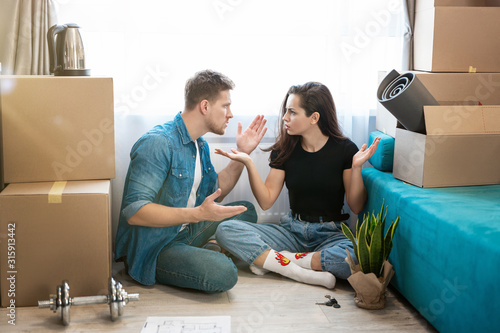 couple man and woman have argument sitting on the floor during unpacking boxes, woman closes her ears, man cries , moving process