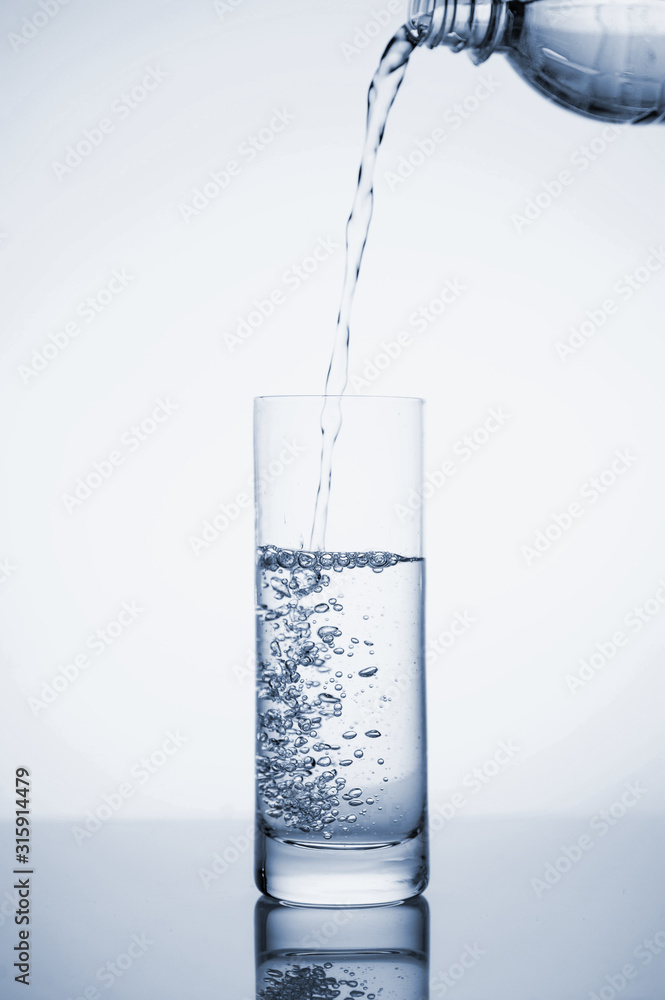 Clear mineral water is poured into a glass with ice. Clear mineral water is poured into a glass with ice.