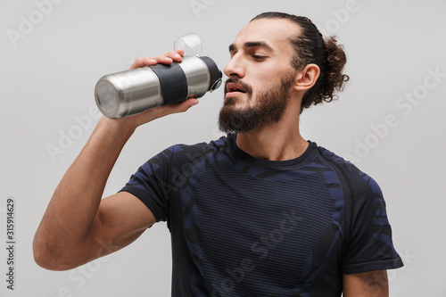 Image of young bearded man in sportswear drinking water