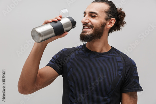 Image of young pleased man in sportswear drinking water and smiling