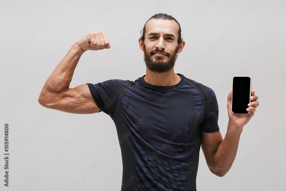 Image of muscular sportsman showing his bicep and holding smartphone Image of muscular sportsman showing his bicep and holding smartphone