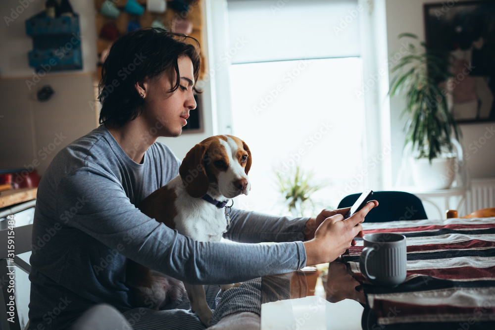 young man with his dog in kitchen at home, morning scene - obrazy, fototapety, plakaty 