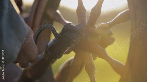 A woman rotates the mechanism to create yarn and fabric on a sunny day on the field.