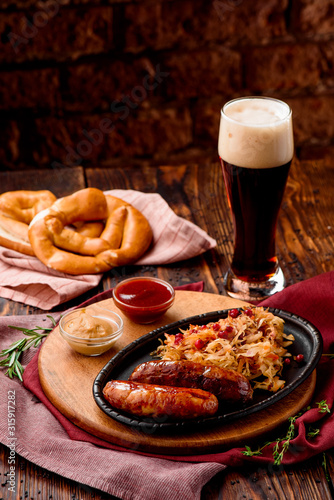 Glass of dark beer with foam and fried sausages with cranberry-honey stewed cabbage served in cast-iron pan
