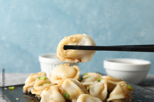 Square plate with dumplings, sauces and chopsticks against blue background, close up