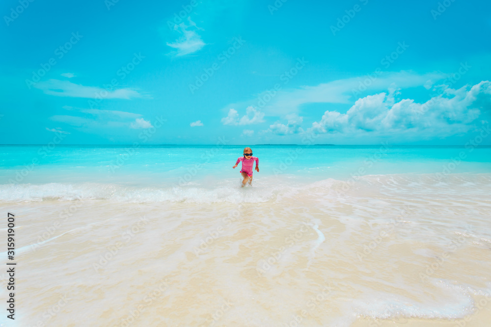 happy cute little girl play with waves on beach