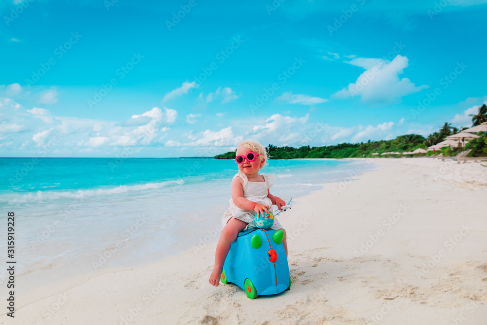 happy cute little girl with luggage and toy plane travel on beach