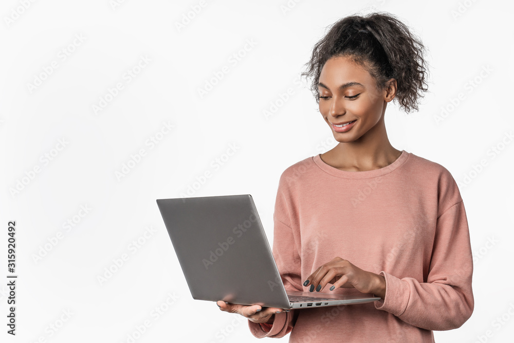 Smiling woman in casual clothes holding laptop and sending email standing over white background Smiling woman in casual clothes holding laptop and sending email standing over white background