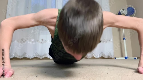 Young skinny thin Man Doing Push Ups. Teenager boy in military form shirt Making Pushups in the room at home. close up cadet training concept. photo