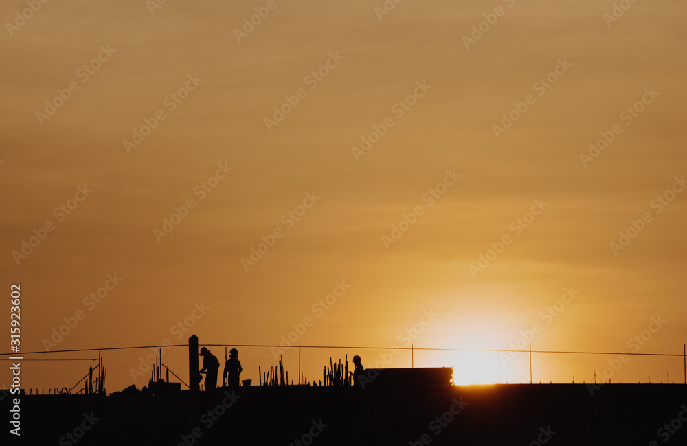 Obraz premium Silhouette sunset construction working and machinery crane hoisting cement mortar mixer bucket container in construction site