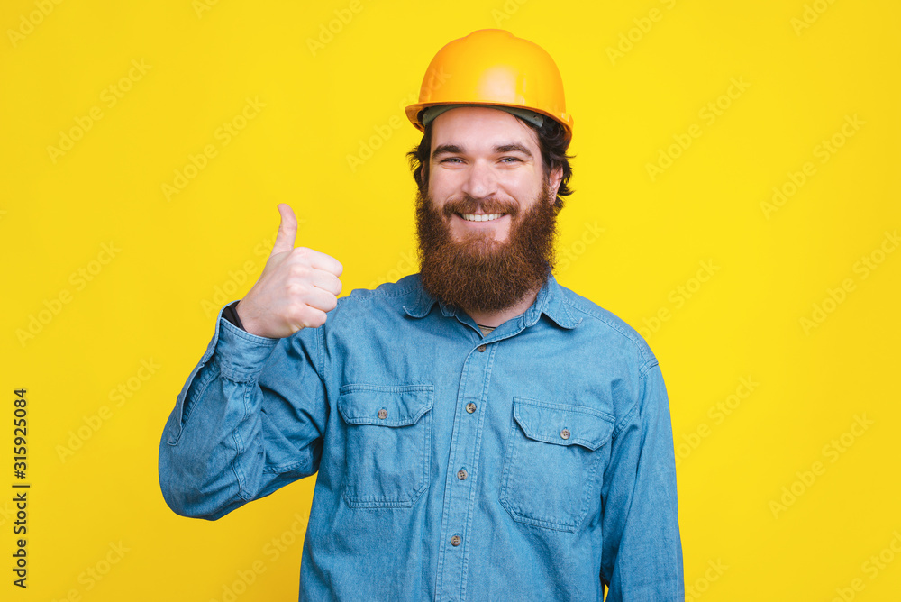 Photo of happy architect showing thumbs up while standing over yellow background