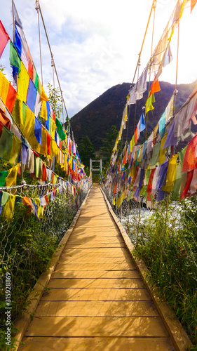 A beautiful view at a long bridge at an river mouth in the Kingdom of Bhutan with buddhist prayer flags and sunshine at day