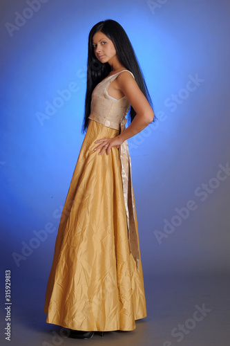 brunette girl in a long golden dress in the studio