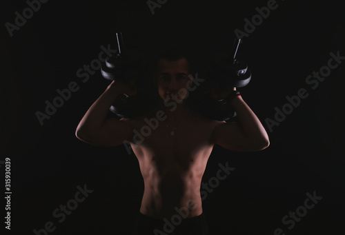 Photo of happy fitness man working with dumbbells over dark background