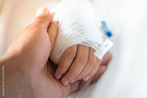 Closeup parent holding child's hand with saline solution to give encouragement.