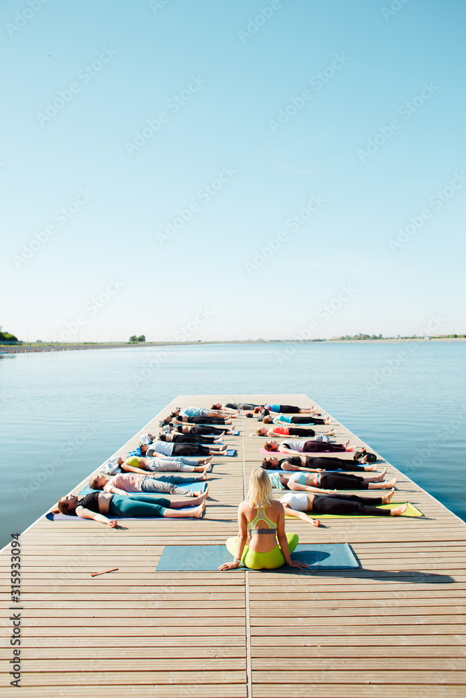 in the morning a group of people do yoga on the pier by the lake