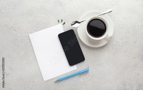 sheet of paper  empty blank  notepad  pen  phone and cup of coffee on gray  concrete background. Planning concept  list  workspace. Flat lay with copy space. Mockup