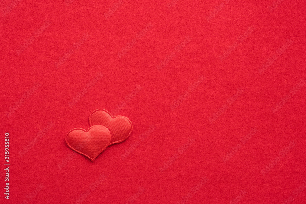 2 small textile red hearts are nearby on a background of red velvet paper.