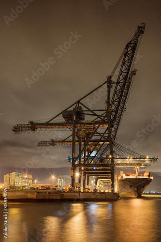 Night scene with illuminated container terminal, massive crane and moored vessel, Port of Antwerp, Belgium.