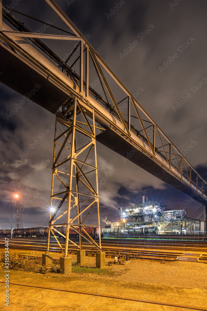 Night scene with illuminated petrochemical production plant and massive pipeline overpass, Antwerp, Belgium.