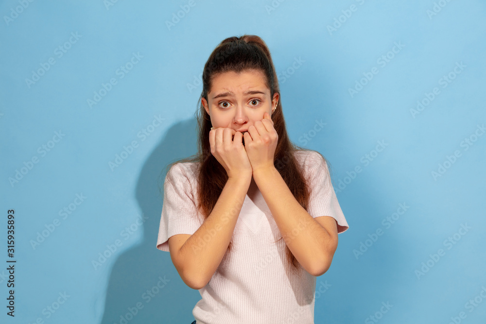 Covering face by hands. Caucasian teen girl's portrait on blue background. Beautiful model in casual wear. Concept of human emotions, facial expression, sales, ad. Copyspace. Looks scared, unhappy. Covering face by hands. Caucasian teen girl's portrait on blue background. Beautiful model in casual wear. Concept of human emotions, facial expression, sales, ad. Copyspace. Looks scared, unhappy.
