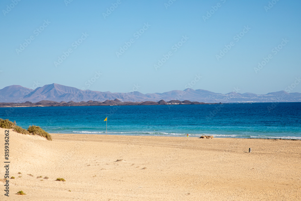 View on sand dune beach from Vuerteventura with Lanzarote and Lobos canary island in the background - golden  yellow sand dunes light blue sky summer season holiday travel vacation seascape mountains