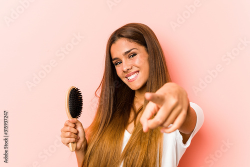 Young caucasian woman holding an hairbrush cheerful smiles pointing to front.