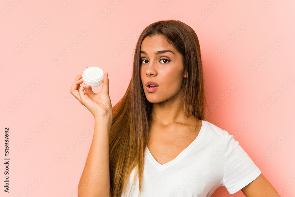Young caucasian woman holding a mousturizer isolated on a pink background Young caucasian woman holding a mousturizer isolated on a pink background