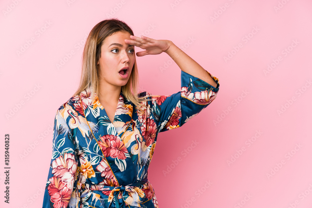 Young caucasian woman wearing pajamas looking far away keeping hand on forehead. Young caucasian woman wearing pajamas looking far away keeping hand on forehead.