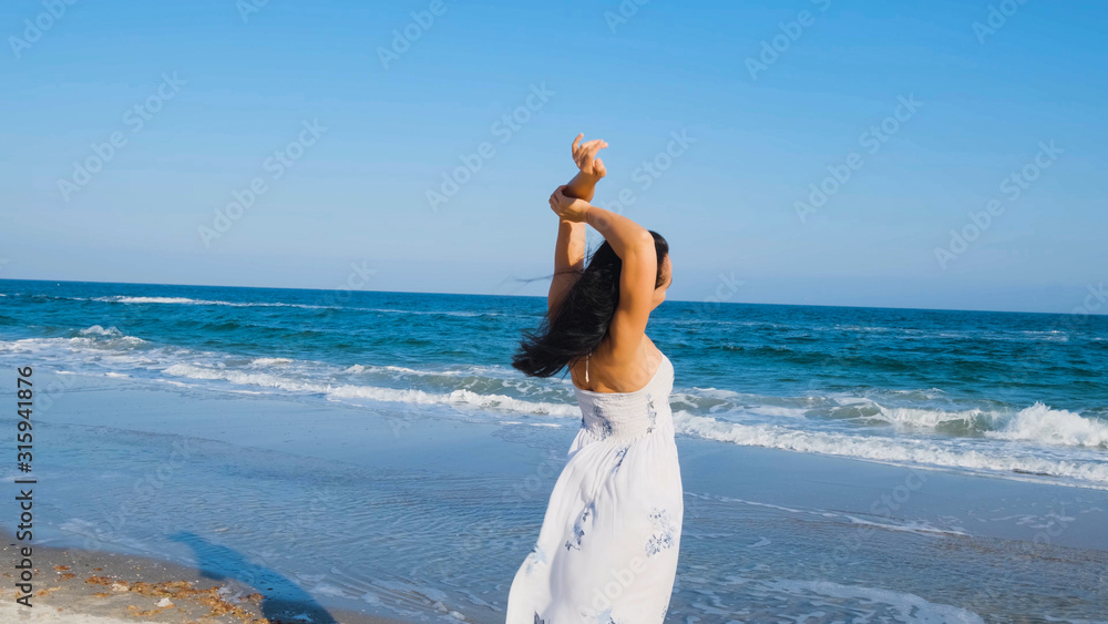 Young beautiful woman dressed in a white dress walk barefoot on the summer beach Young beautiful woman dressed in a white dress walk barefoot on the summer beach