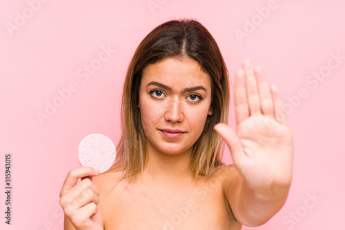 Young caucasian woman holding a facial disk isolated standing with outstretched hand showing stop sign, preventing you.
