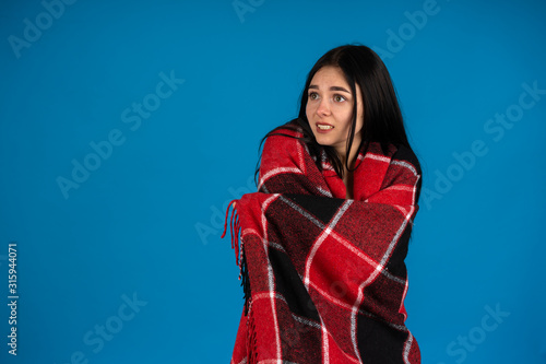 Upset girl wrapping in warm checkered blanket isolated on blue background