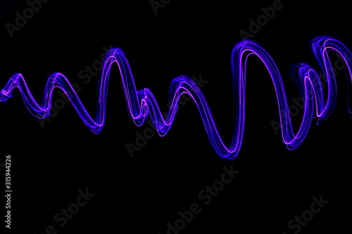 Long exposure light painting, vibrant purple color in abstract swirl against a clean black background. Light painting photography.