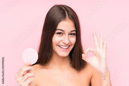 Young caucasian woman holding a facial disk isolated cheerful and confident showing ok gesture.